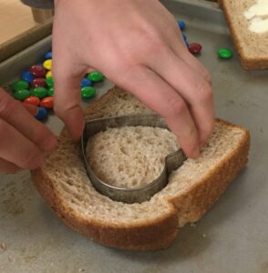 a girl using a heart shaped cookie cutter to cut a heart out of the sandwich