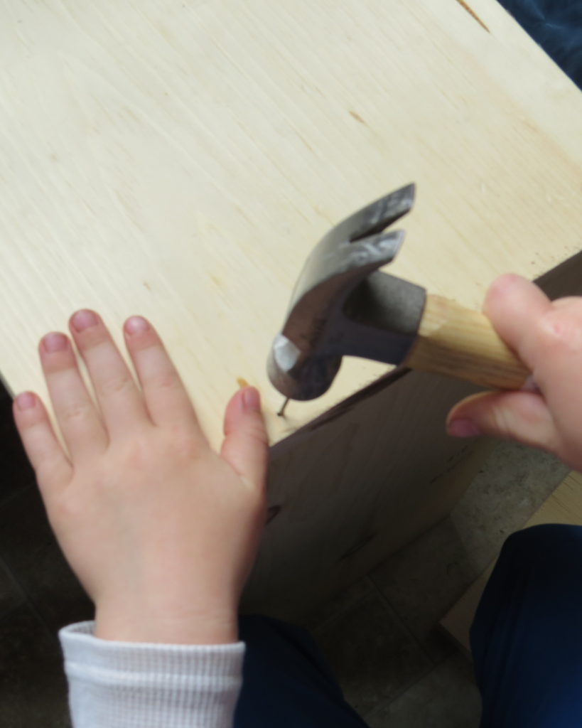 a child hammering in a nail into his shelf building project for kids